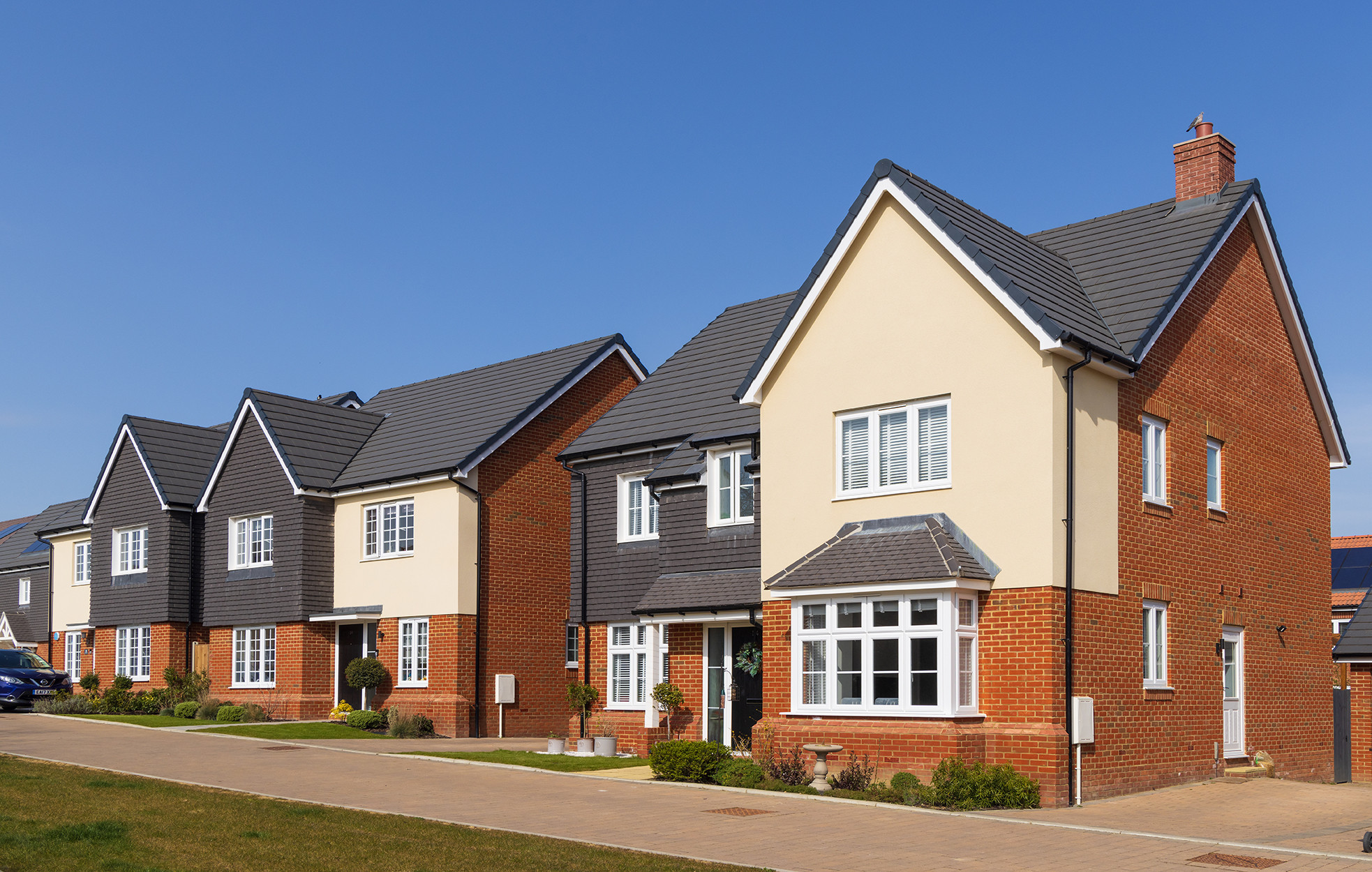 A row of modern brick houses with gabled roofs and manicured lawns under a clear blue sky.