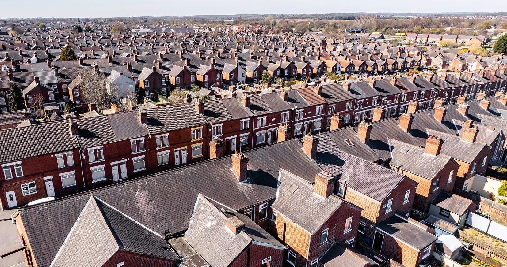 Aerial view of a densely populated residential area, showcasing rows of red brick houses with varying roof styles and greenery.